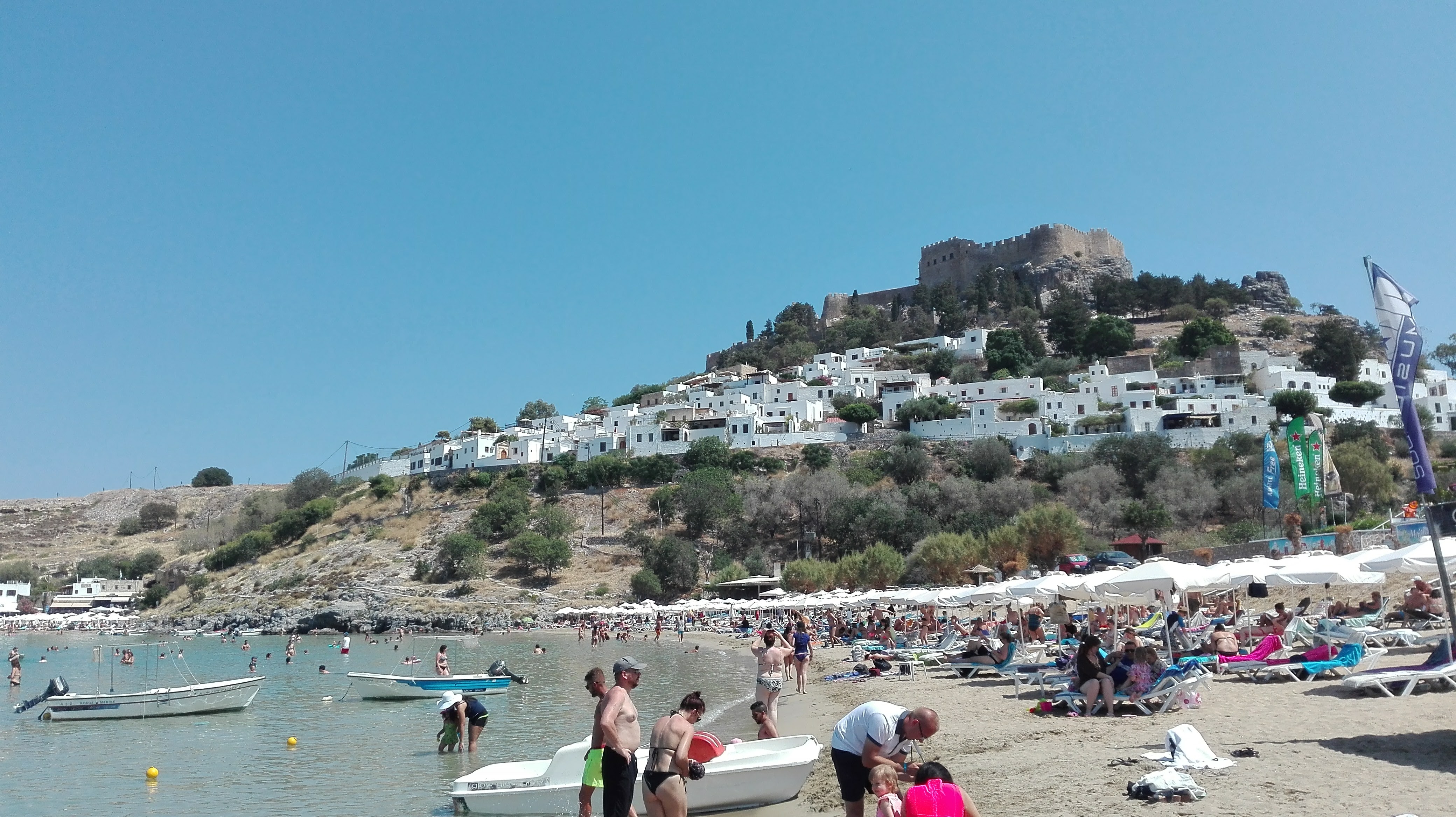 On the beach under the city of Lindos city. As you can see the beach is full of tourists, just as the small city.
